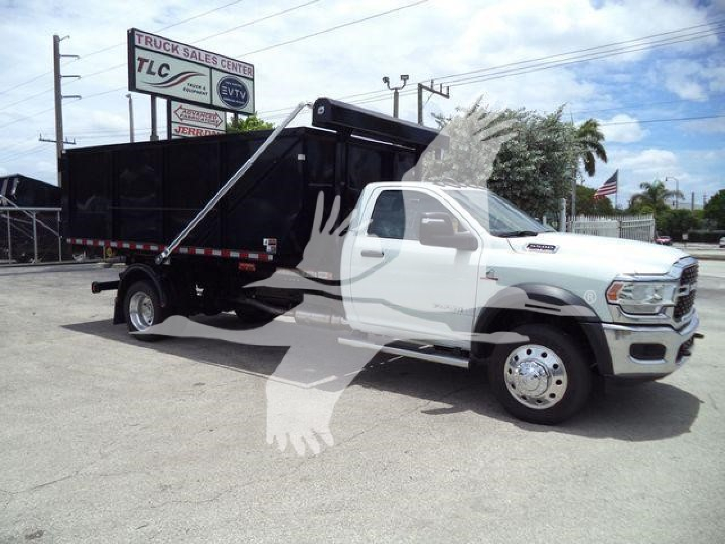 Ram 5500 dump truck with black dump bed, white cab, chrome wheels, and a logo watermark overlay. Visible text includes dealership sign in background with TLC Truck Sales Center, and a banner reading something like 'DSL' on the stock board.