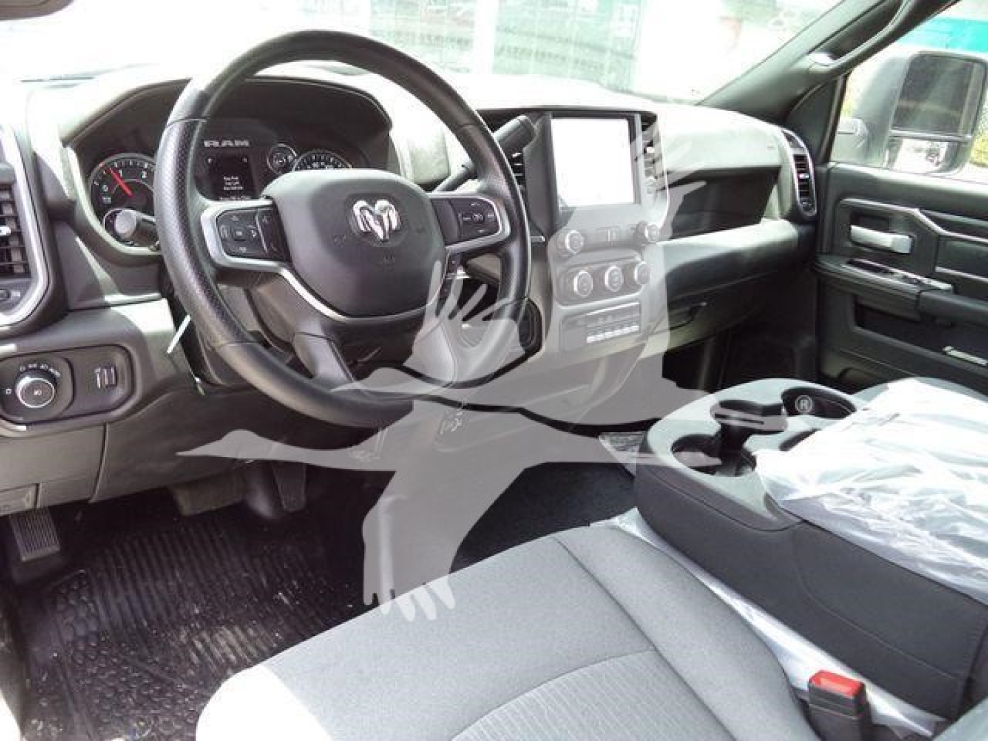 Ram truck interior overview showing steering wheel with Ram logo, dashboard, large central infotainment screen, gear selector console, and front seats in cabin view.