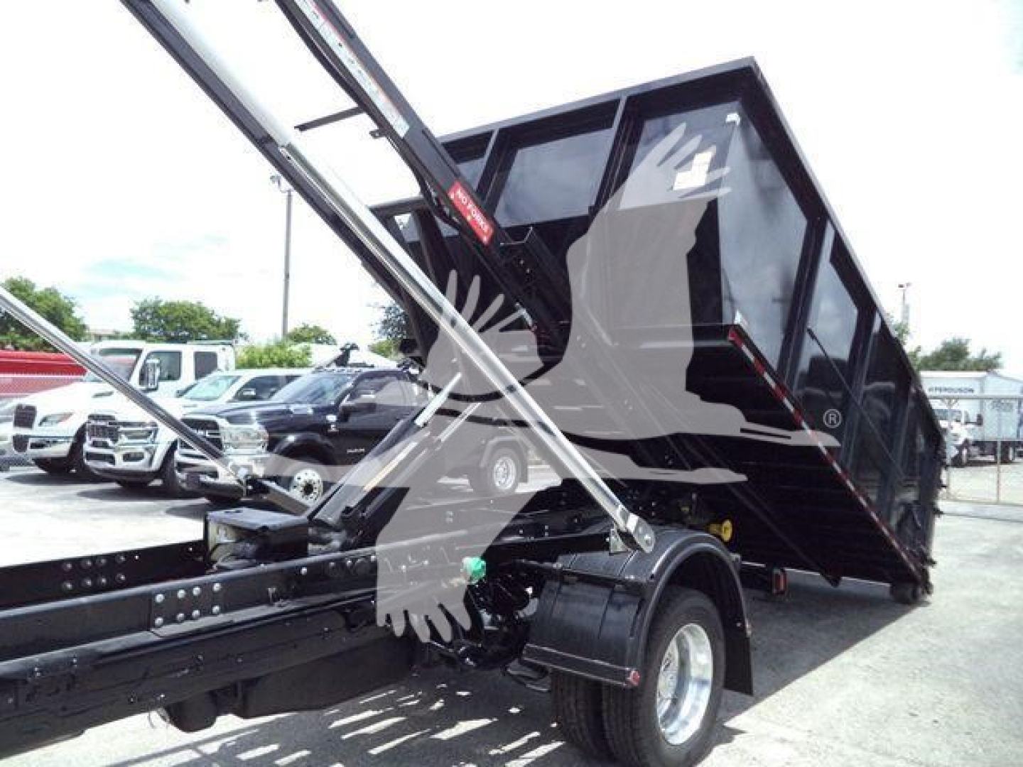 Truck bed tilting with hydraulic lift on a Ram 5500 chassis in a roll-off configuration; black dump bed raised over rear wheels.