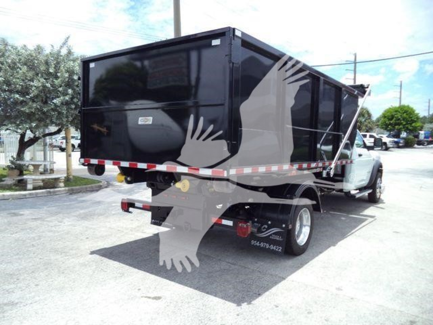 Ram 5500 dump bed truck in a lot showing the rear and side with a black dump body and white Ram cab; some signage and contact numbers on the rear wheel area.