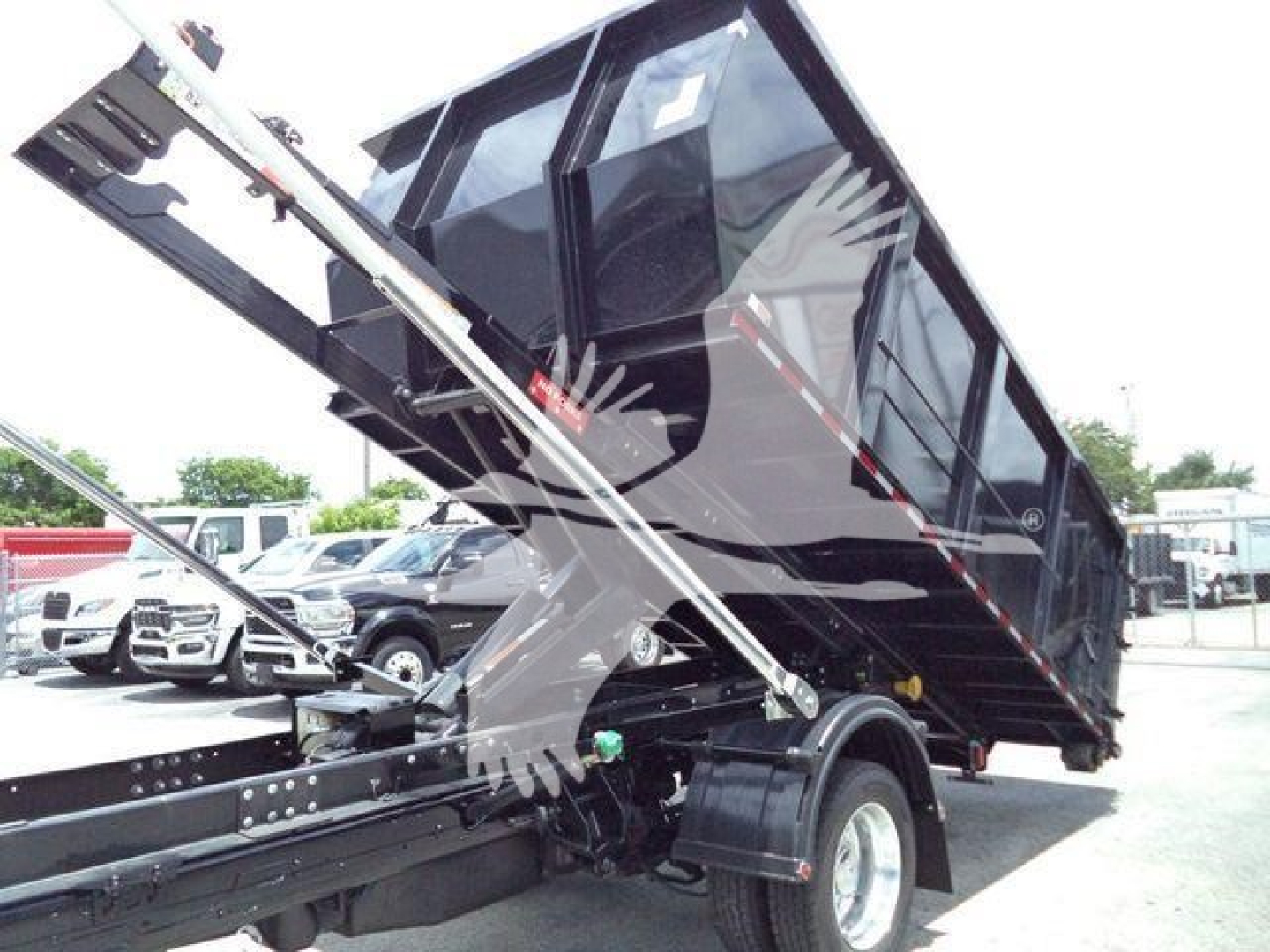 Ram 5500 dump truck bed in elevated position attached to a roll-off body with hydraulic arms visible.