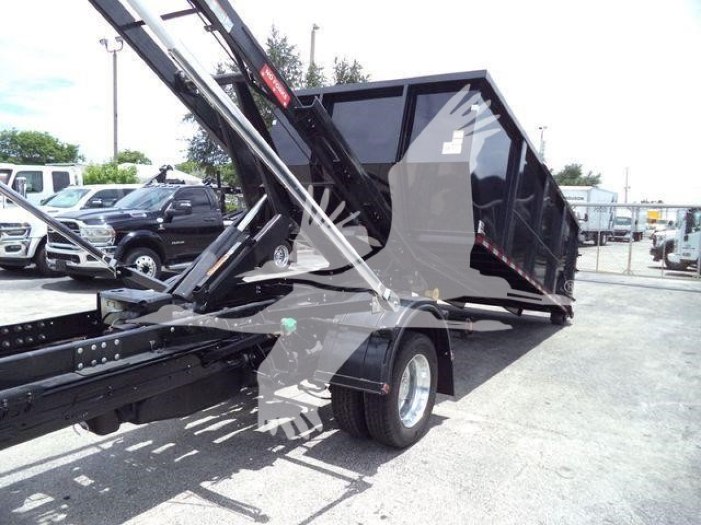 Ram 5500 roll-off truck with black dump bed and hydraulic arm, side view showing rear wheel and trailer hitch.