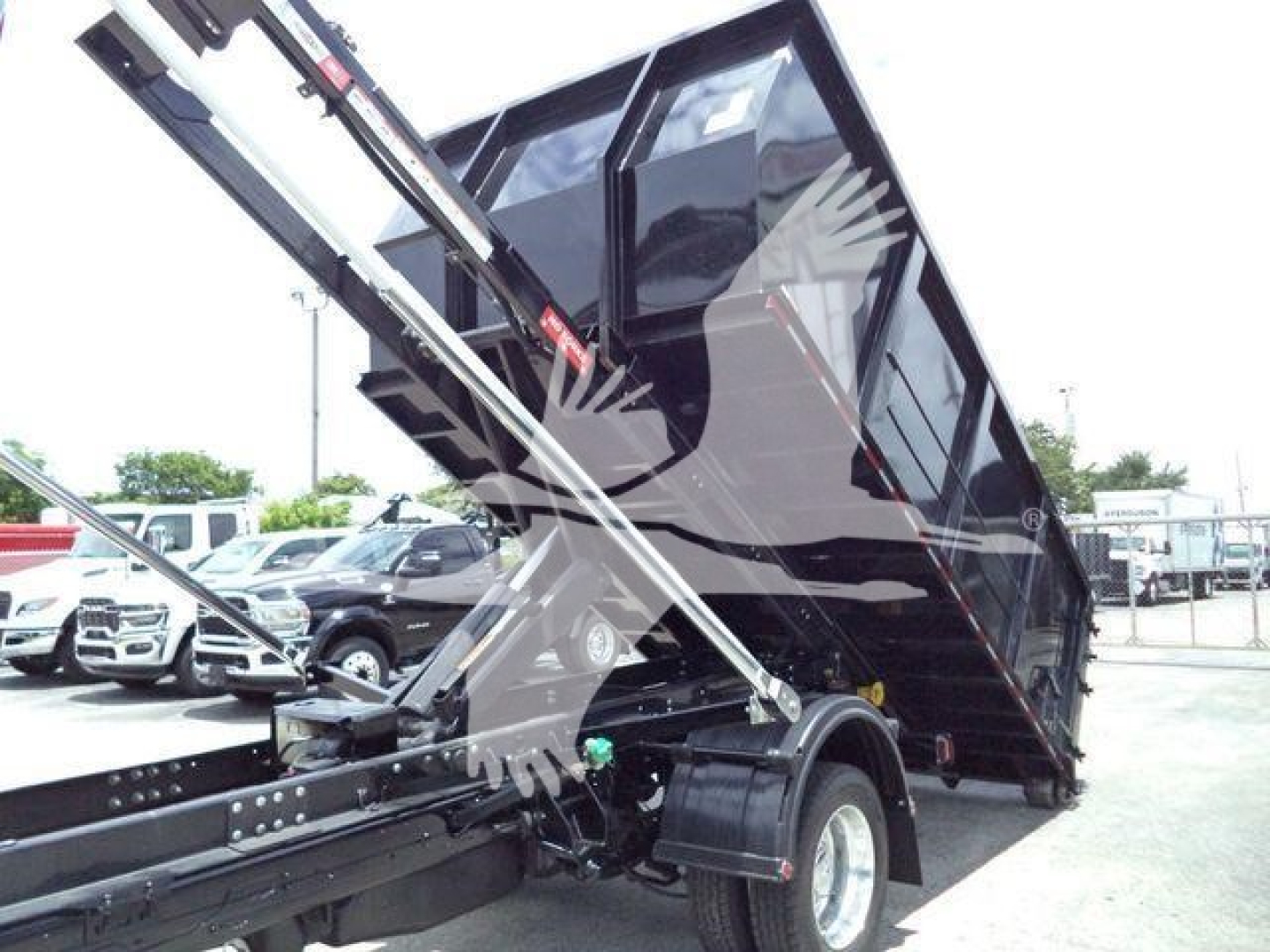 Ram 5500 roll-off truck bed on a tilt in a dealership lot showing hydraulic lifting arms and black cargo bed.