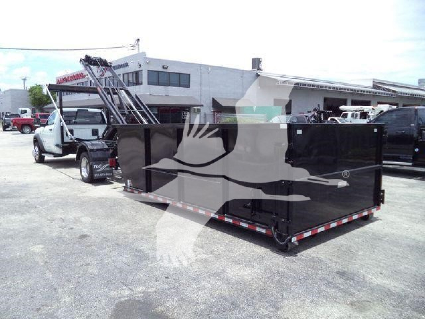 Ram 5500 rear view showing a large black dump or roll-off container attached to a truck, with a white cab in background.