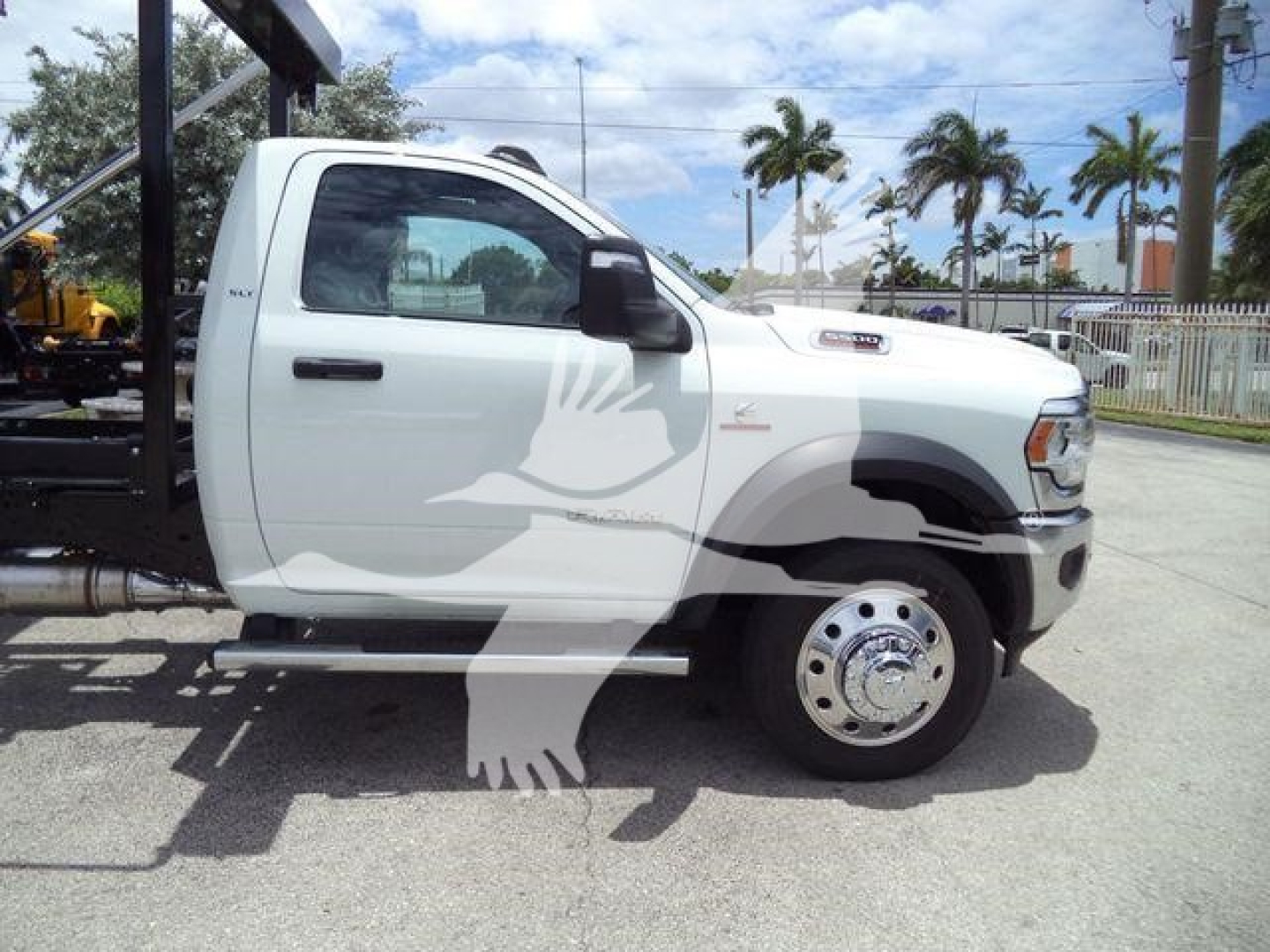 Truck side view showing cab and front wheel of a white Ram 5500 roll-off truck with black fender accents and a bird decal on the door; no legible model stickers visible