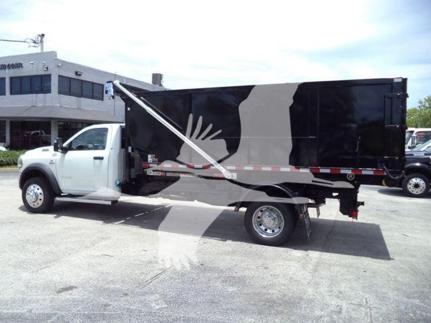 Truck side view showing a white Ram 5500 SLT dump body with black/gray graphic design, stock number DSL550014SNG2, roll-off category, new condition.