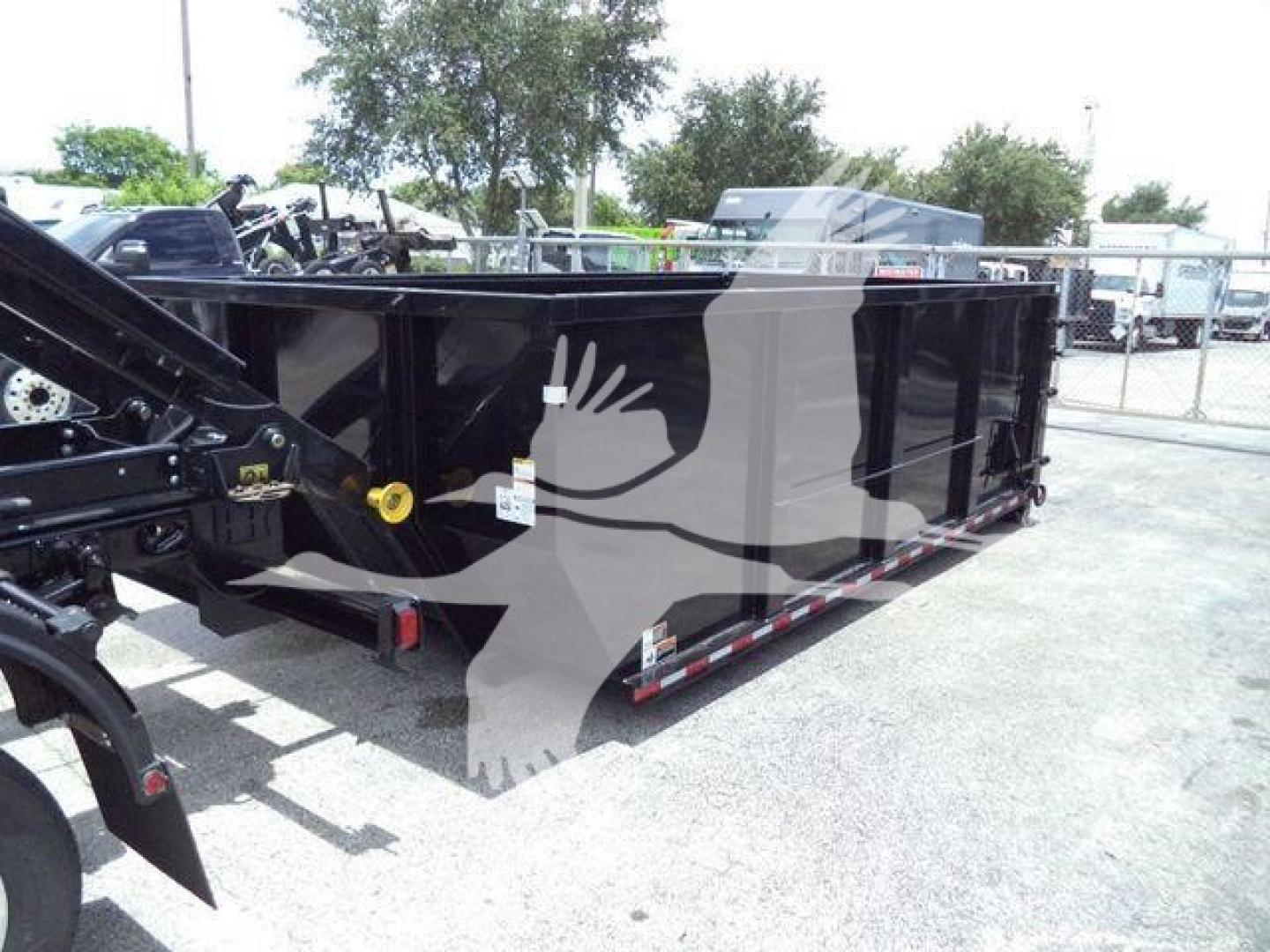 Ram 5500 SLT roll-off truck bed in a dealership lot with black finish and safety rails, side view showing tie-down hooks and hydraulic components.