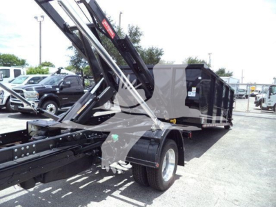 Ram 5500 bed with roll-off hoist system, front wheel and chassis visible; cargo bed side panels and hydraulic arms visible.
