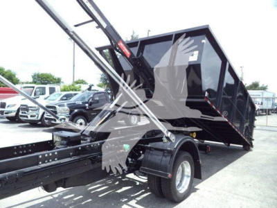Truck bed with roll-off hoist and black dump body mounted on a Ram chassis showing hydraulic arms and wheel. Visible text on sticker and components.