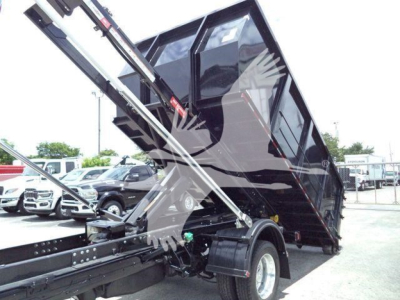 Ram 5500 roll-off truck bed on a tilt in a dealership lot showing hydraulic lifting arms and black cargo bed.
