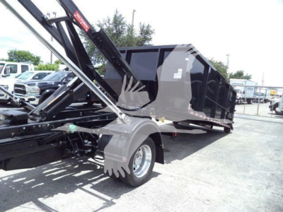 Ram 5500 SLT dump/roll-off truck body with hydraulic lift arm and dual rear wheels, side view showing cargo bed and hydraulic components.