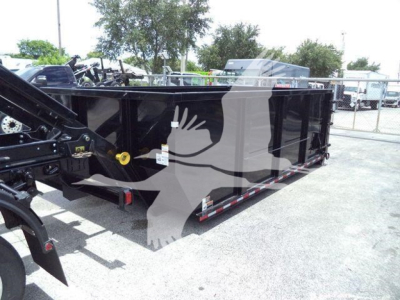 Ram 5500 SLT roll-off truck bed in a dealership lot with black finish and safety rails, side view showing tie-down hooks and hydraulic components.
