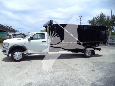 RAM 5500 SLT-based roll-off truck with white cab and black dump body, side view showing dual rear wheels and hydraulic bed tilt mechanism.