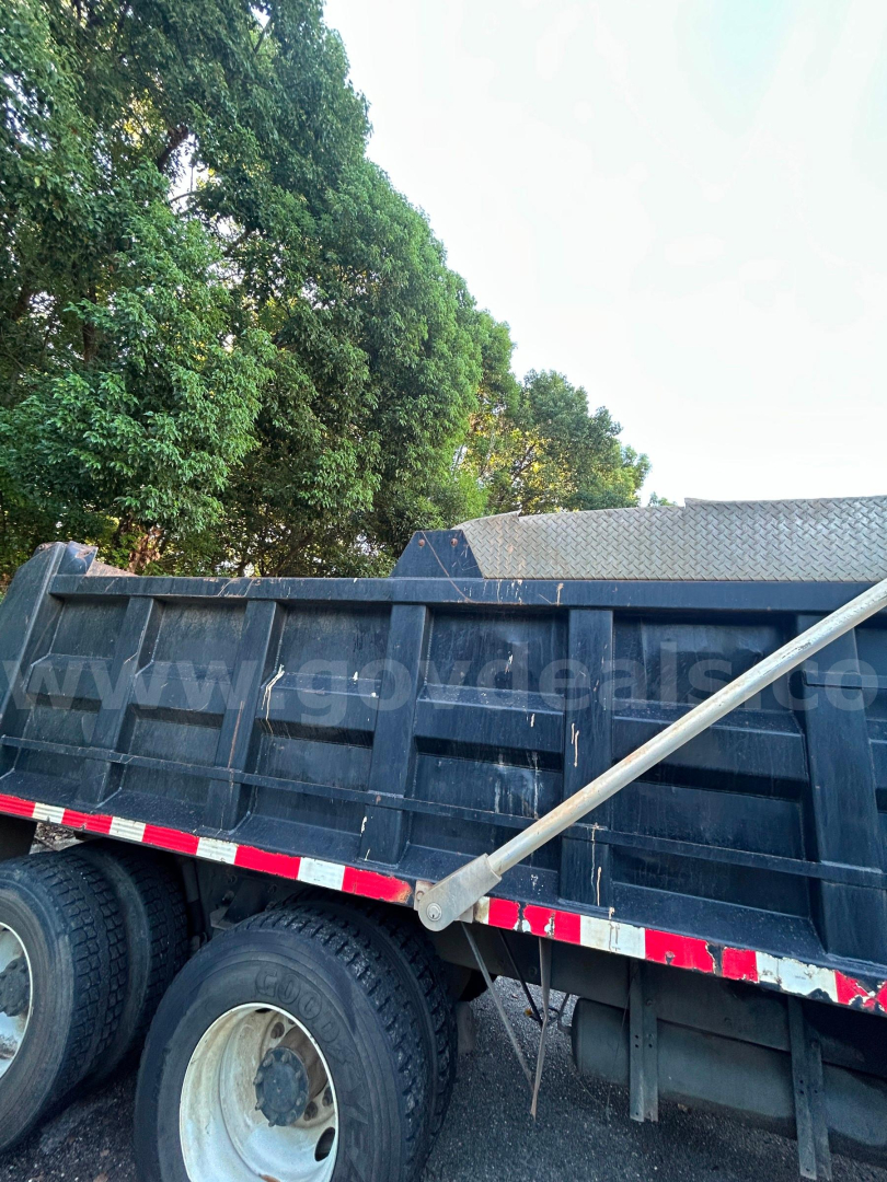 Dump truck bed and wheels of a 2016 Kenworth T370 dump truck showing the side with a long aluminum support bar across the top edge.