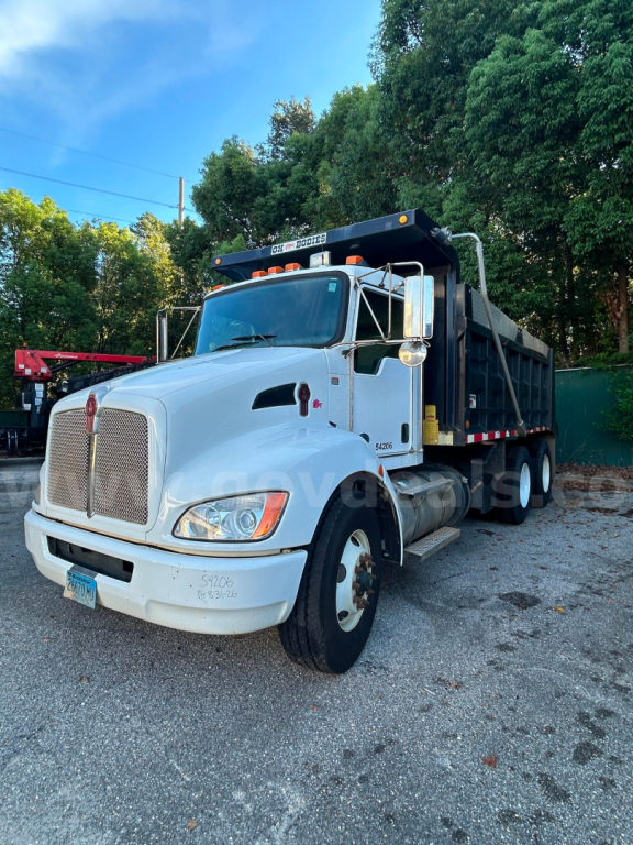 Kenworth T370 dump truck in white with black dump bed, front grille, and overhead hydraulic system. Visible side mirrors, headlamps, and Kenworth badge on the front.