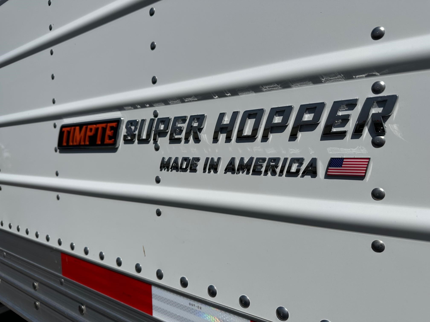 Timpte Super Hopper trailer side badge reading TIMPTE SUPER HOPPER MADE IN AMERICA with small American flag, riveted metal panels.