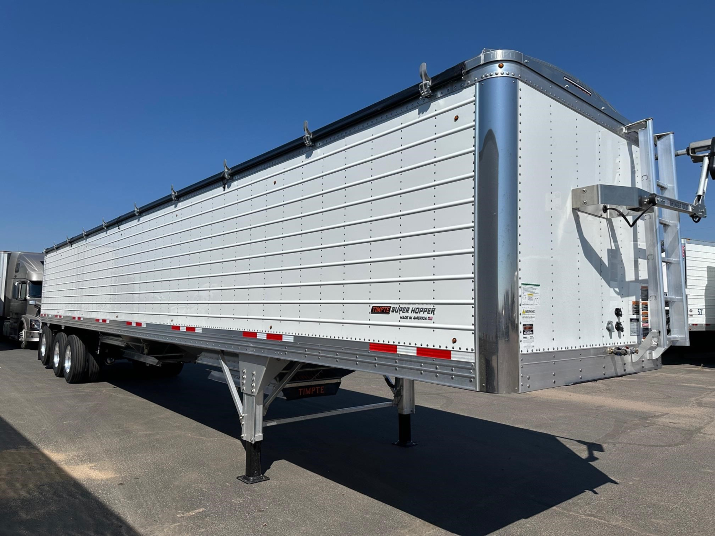 Timpte Super Hopper trailer in silver with side panels and front neck area; multiple axles visible under trailer; rear lowering legs; reflective tape along lower edge.