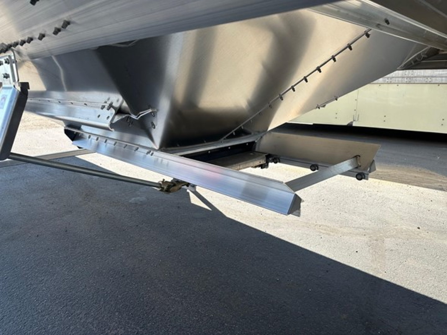 Timpte Super Hopper trailer undercarriage showing metal frame, support legs, and discharge auger area with welded joints and shiny aluminum surface.