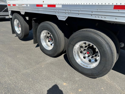 Trailer wheel ensemble of a Timpte Super Hopper showing three polished steel wheels and tires under a silver side rail container.