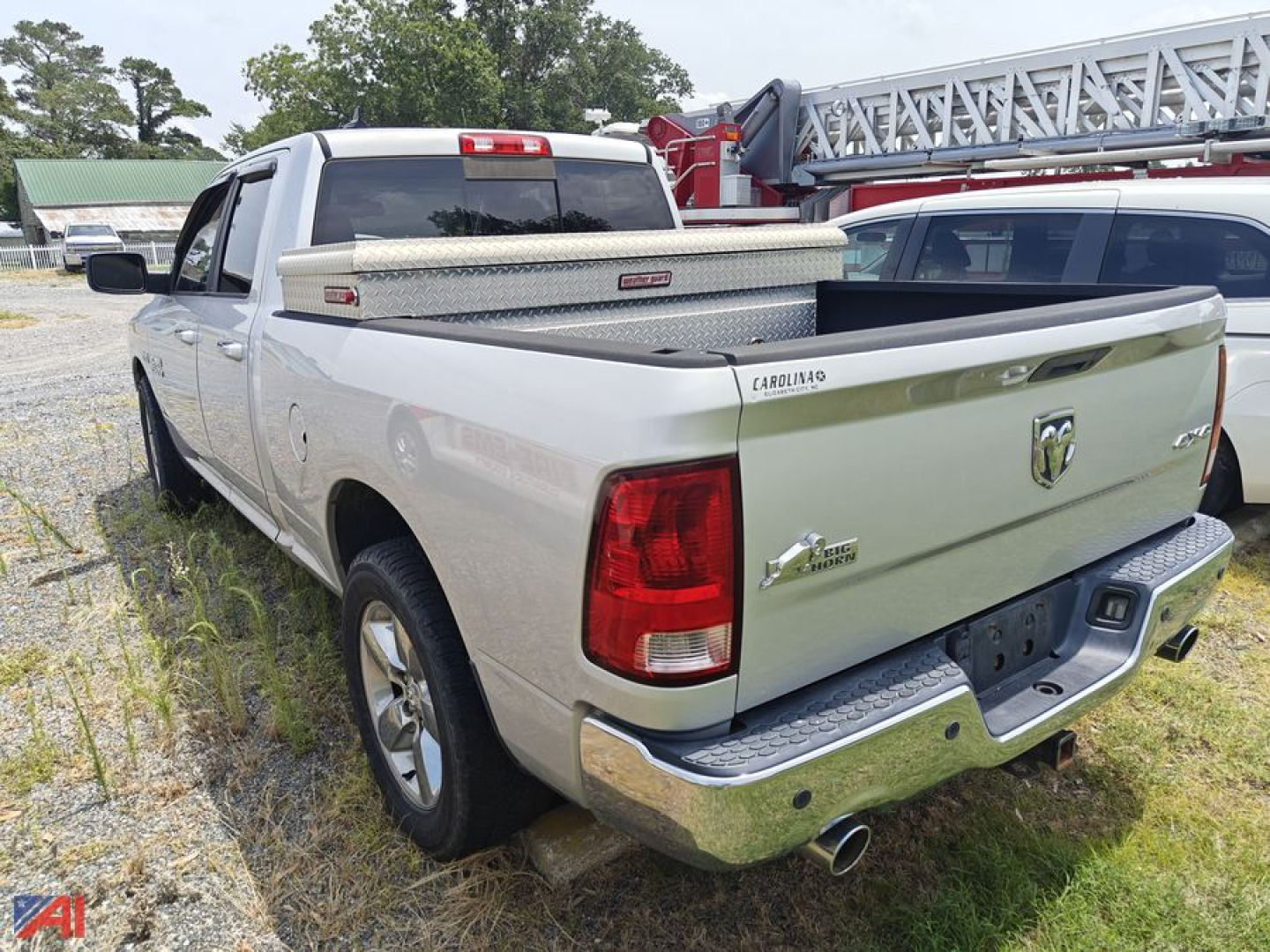 2013 Ram 1500 quad cab pickup rear view showing truck bed and toolbox in a salvage yard.