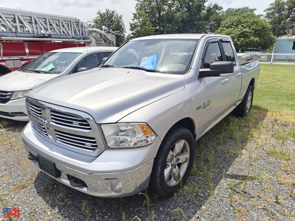 Ram 1500 pickup truck extended cab 2013 silver/gray front three-quarter view parked on gravel lot with ladder rack in background and blue notice on windshield.