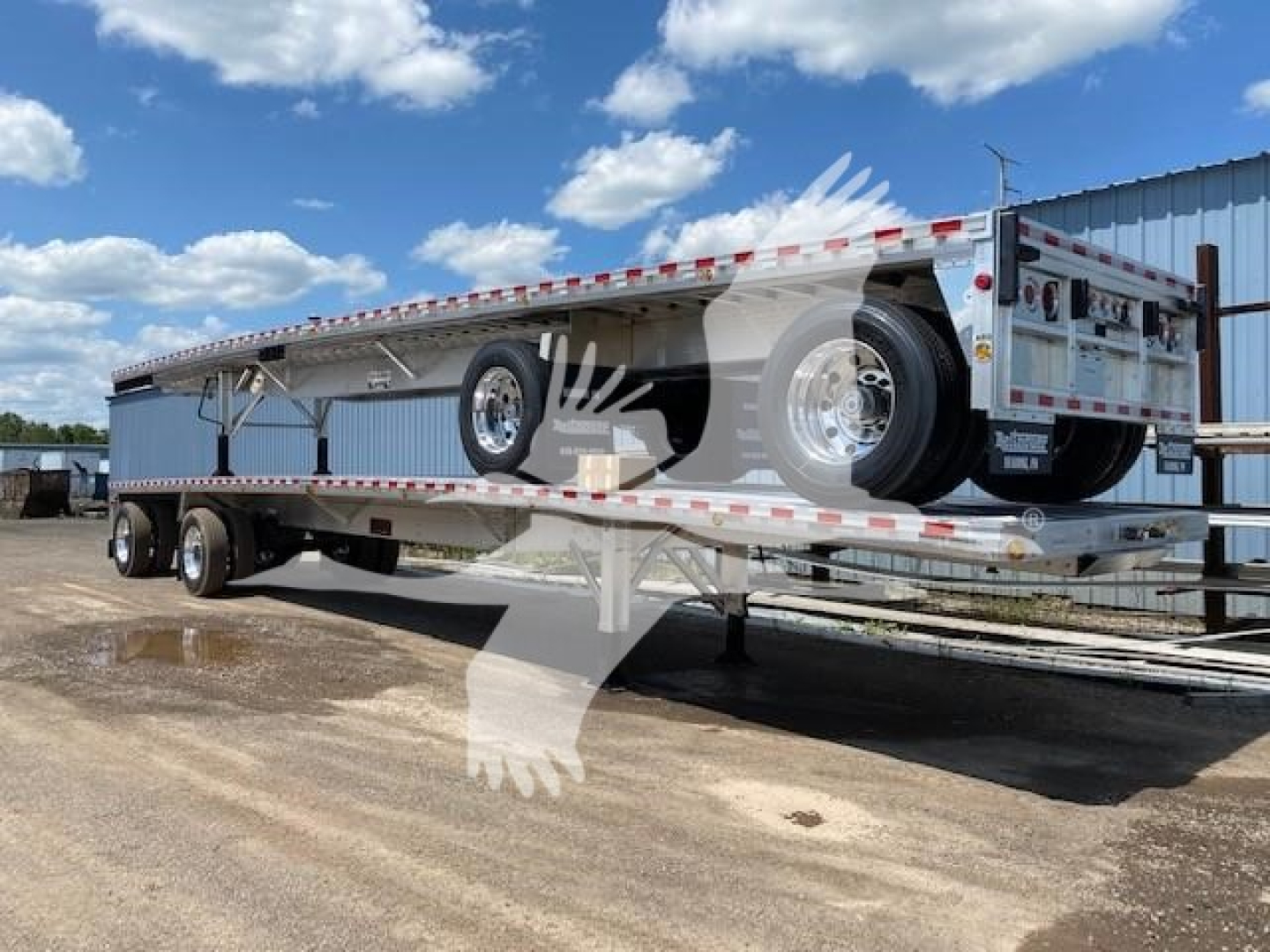 Flatbed trailer in service position showing long aluminum deck, tandem axles, and rear ramps; side rails and reflective tape along the perimeter; model name Big Bubba on trailer bed.