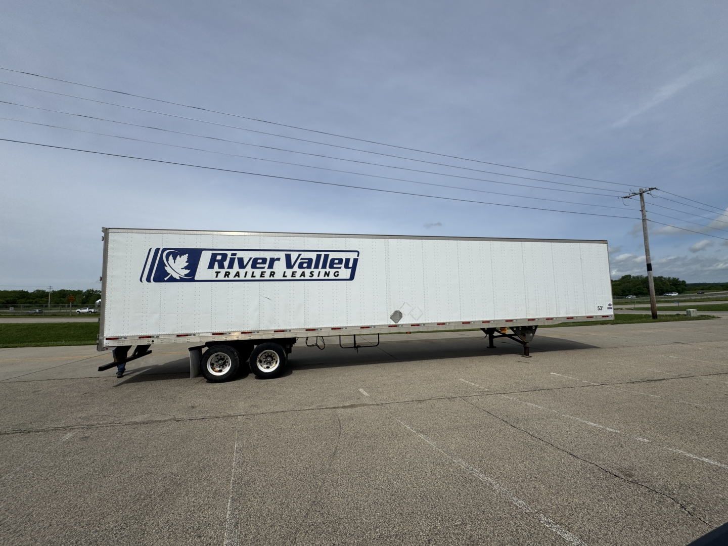 Long white River Valley trailer with logo and text, side view, parked on asphalt.