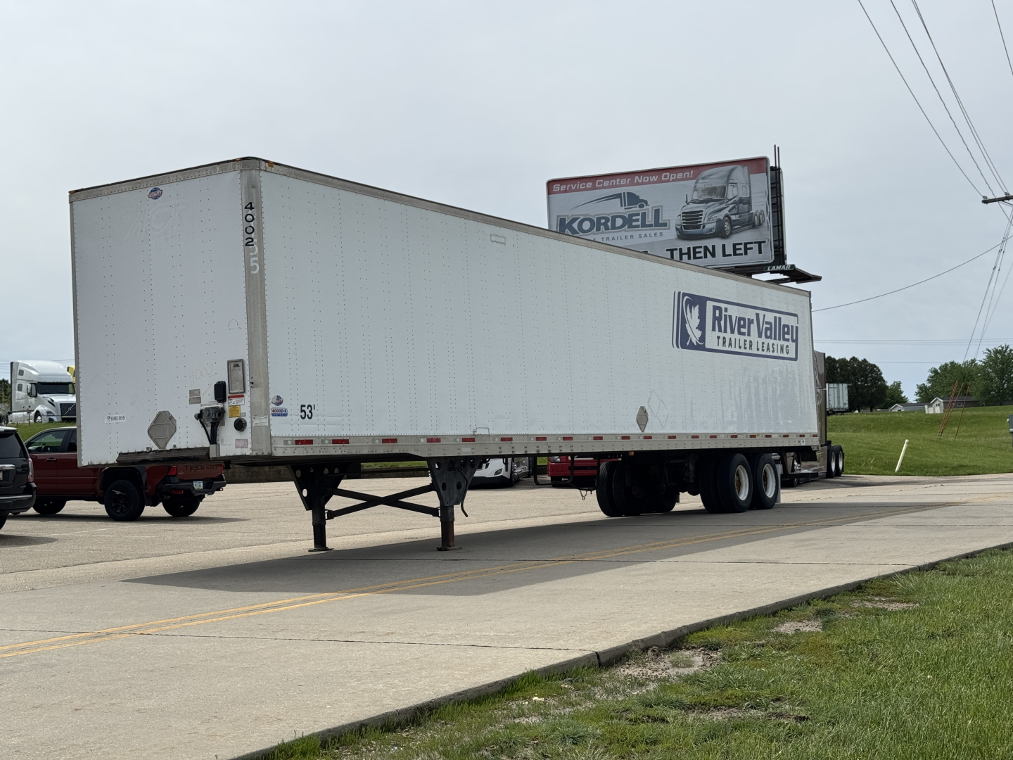 Trailer with River Valley Trailers logo and a Kordell billboard in background. White 53' box trailer on dual rear axles, front landing gear visible. Side text shows 53'.