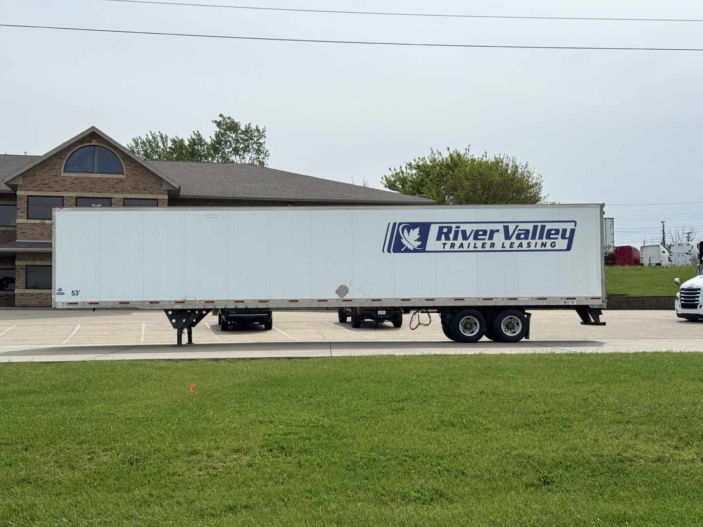 Trailer side showing River Valley Trailers Leasing logo on a white utility trailer with a raised cab in the background.