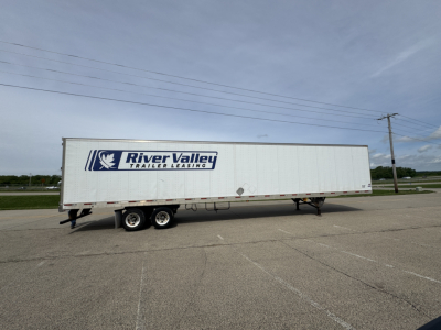 Long white River Valley trailer with logo and text, side view, parked on asphalt.