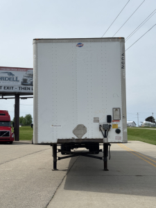 Trailer rear view showing back of a white utility 4000Dx trailer with lighting, bumper, and dual hitch area; includes VIN and stock numbers in image context.