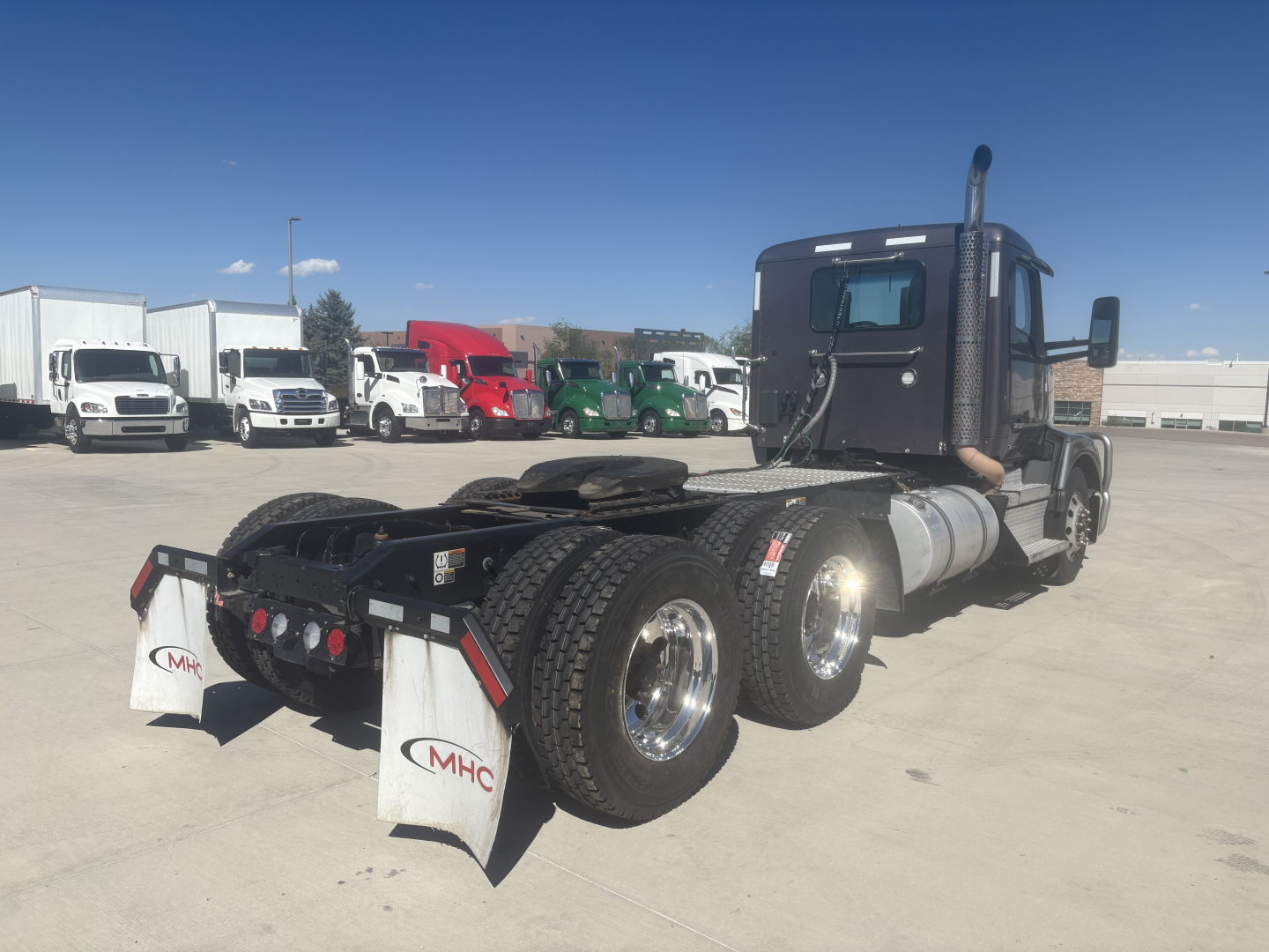 Kenworth T680 daycab truck chassis showing rear twin-axle configuration and fifth wheel, with multiple trucks in background.