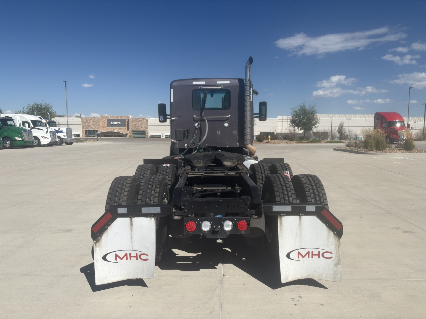 Kenworth T680 rear view showing dual mud flaps with MHC logos and chassis with fifth wheel and hookups.