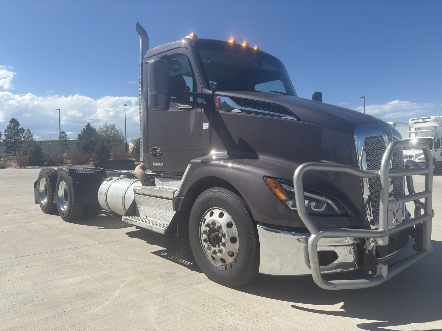 Kenworth T680 conventional daycab truck, dark brown exterior, front bull bar, chrome bumper, side steps, dual rear axles visible, VIN sticker not legible.