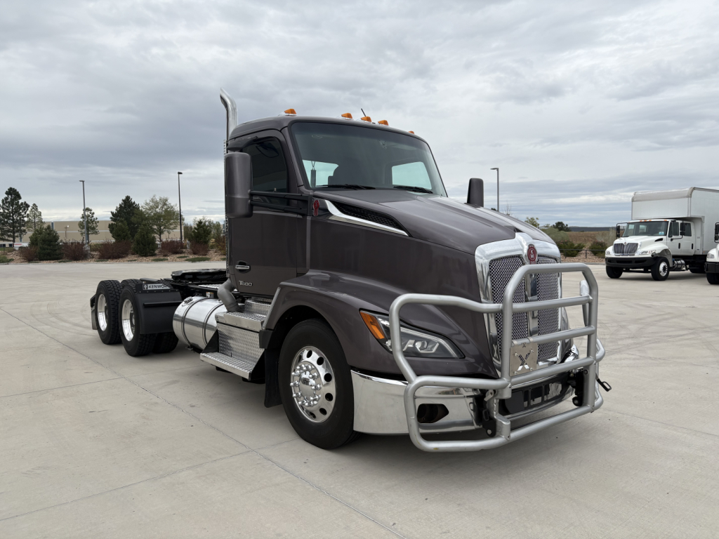 Kenworth T680 truck tractor in a parking lot, front grille guard, side view shows chrome bumper and dual rear axles, with no text visible on panels.