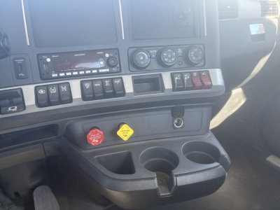 Kenworth T680 dash center showing controls, radio, climate dials, and red/blue warning knobs; cup holders and storage tray visible.