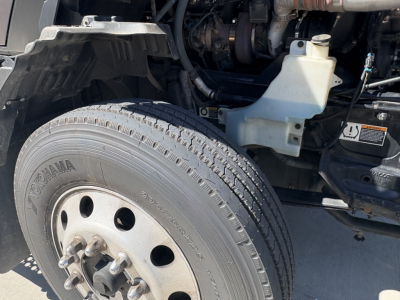 Kenworth T680 engine bay side showing front tire with Yokohama tire and wheel, coolant reservoir, battery area, and engine components visible.