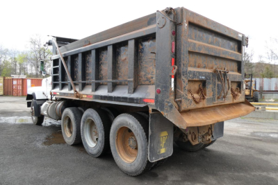 Dump truck rear three-quarter view showing dump bed and dual rear wheels with mud flaps and weathered metal sides.