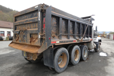 Dump truck dump bed and rear view of a 2000 Mack RD688S with rusty but legible rear tailgate and triple axle wheels.