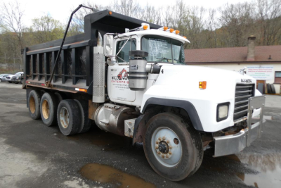 Dump truck showing Mack RD688S with white cab and black dump bed, front view angled, side label panels visible.