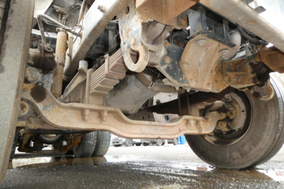 Underbelly view of a Mack RD688S dump truck showing front suspension, exhaust and driveshaft components with dirt and grime.