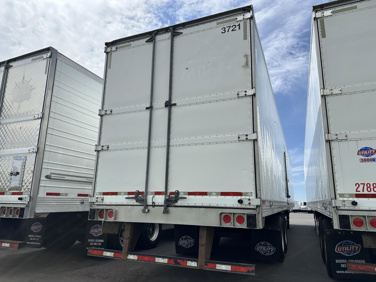 Rear view of a used Utility 3000R trailer with tandem doors and rear hinges, showing metal panels and rear bumper under clear sky.