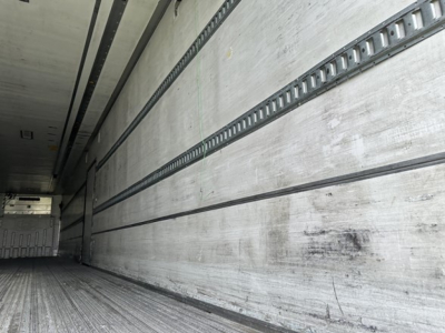 Reefer trailer interior showing long aluminum side walls with horizontal E-track rails and worn floor at interior rear of trailer.
