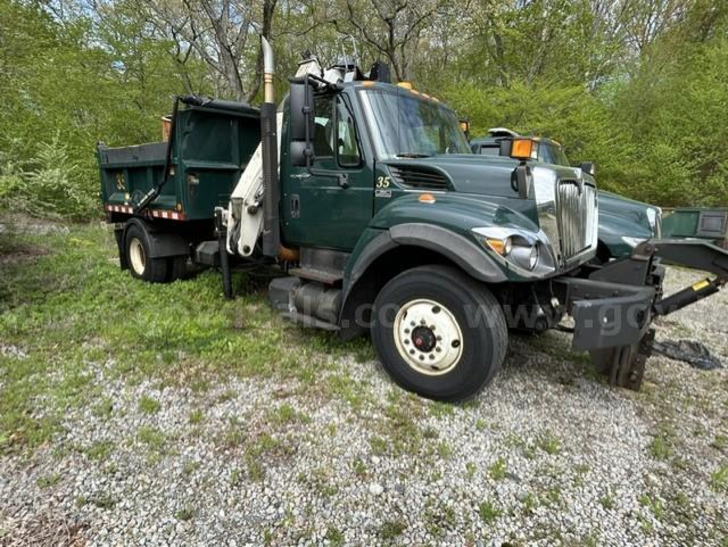 Truck cab and dump body of a 2012 International 7400 WorkStar dump truck with green paint and white wheels, side view showing front grille and crane arm.