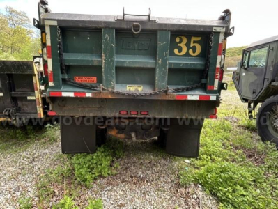 Dump truck rear showing '35' on tailgate and two mudflaps, with vegetation on ground and gravel.