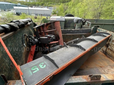 Dump truck bed viewed from side showing hydraulic system and spreader equipment, with large chute and metal rails inside cargo area.