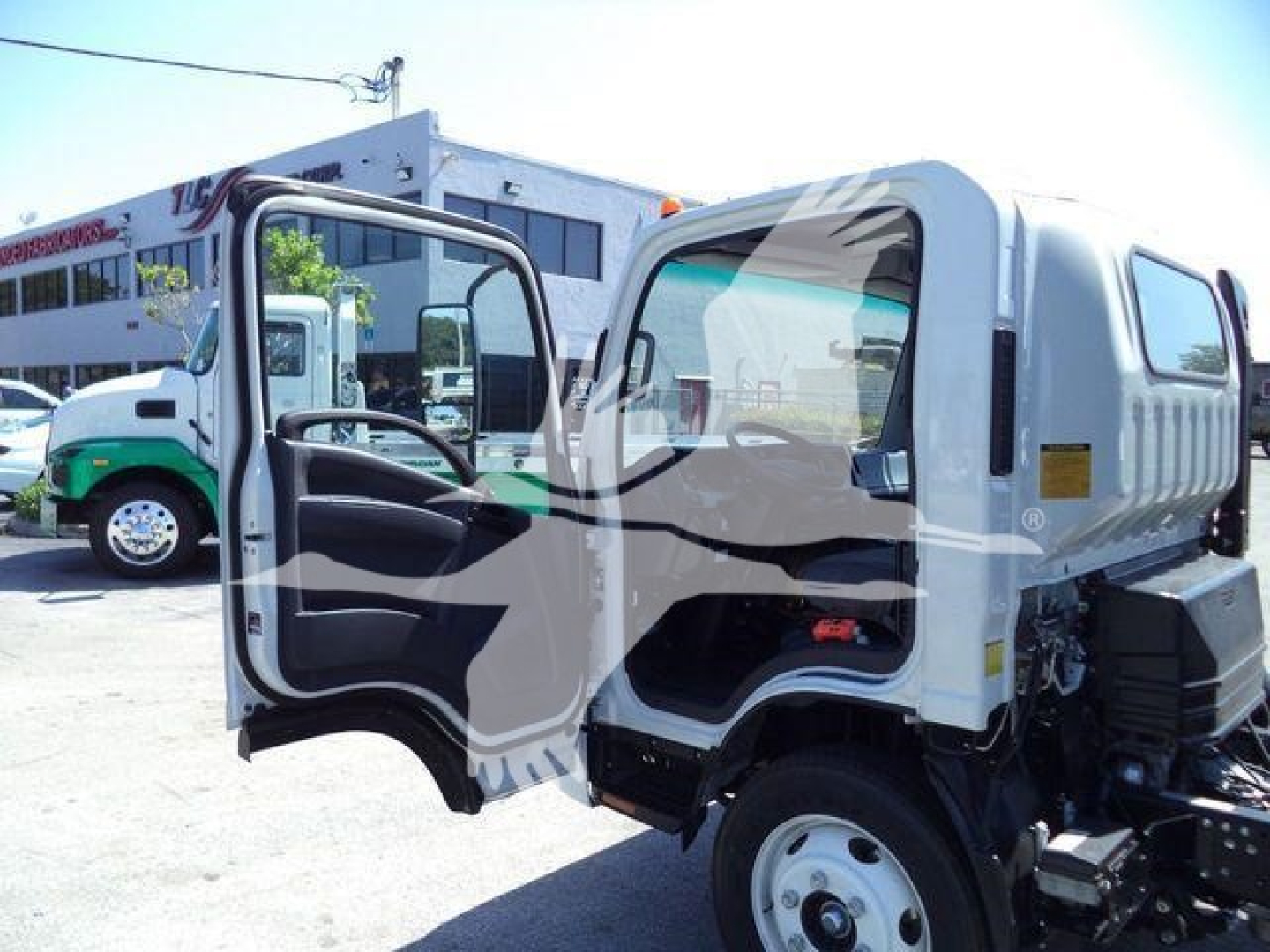 Isuzu NPR HD cab open showing interior and dashboard with a white cab and chassis in a dealership lot.