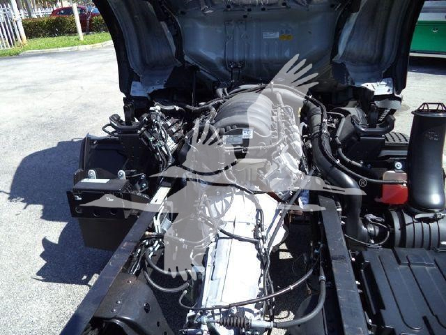 Isuzu NPR HD truck engine bay view with exposed components and wiring under open hood; front frame rails visible.