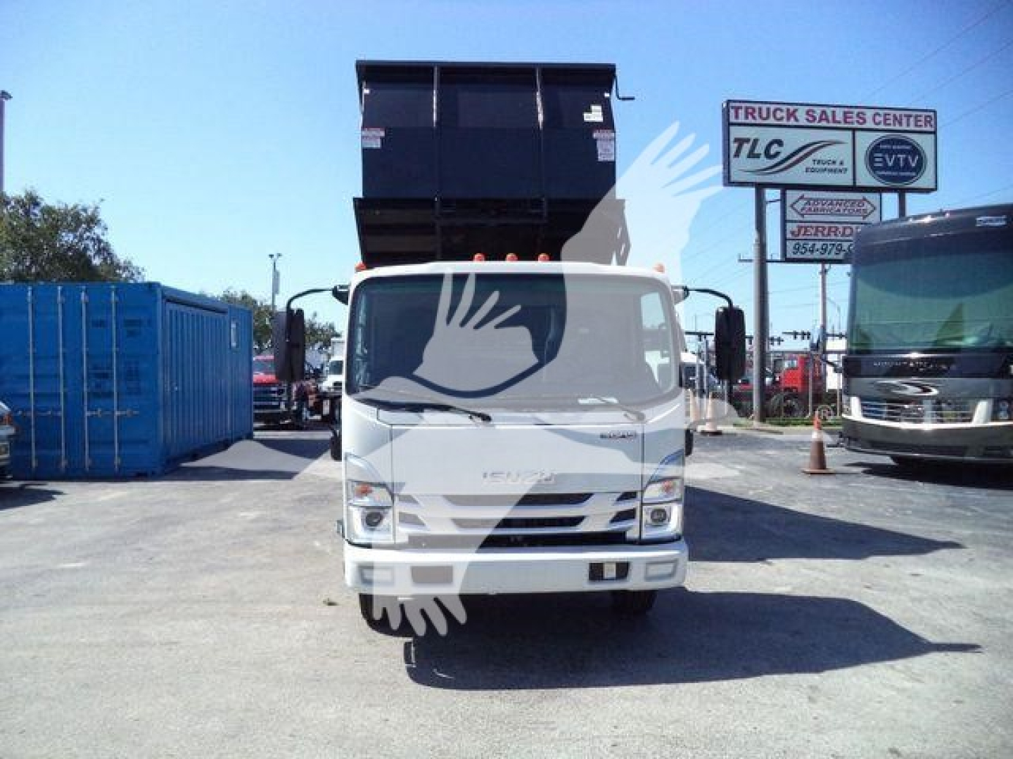 Isuzu NPR HD light truck in a lot with a raised dump bed, front view. Visible signage in background includes 'TRUCK SALES CENTER' and other signs. White cab with black dump bed raised high.