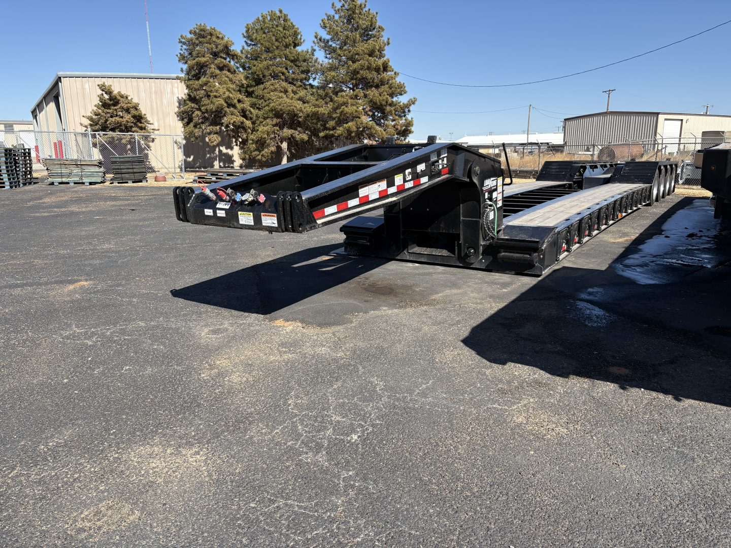 Load King 554-Quad-9' Wide 24' LDH trailer in a парков area, showing lowboy trailer with black frame and reflective red/white stripes.